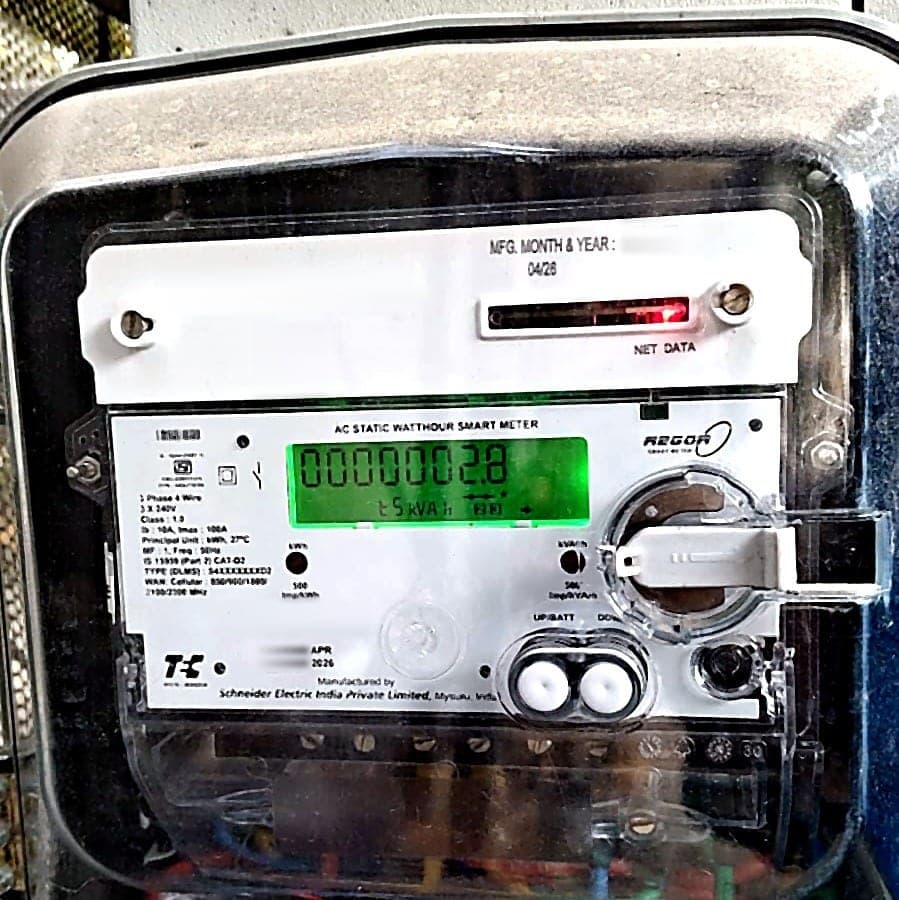 A three-phase DLMS smart meter mounted inside a transparent weatherproof enclosure, its green display showing a cumulative energy reading.